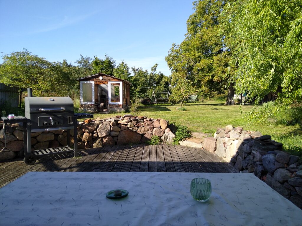 Terrasse mit Sitzgruppe, Hollywoodschaukel und Grill, im Hintergrund Gartenhäuschen und Hof